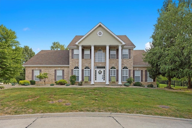 neoclassical home with a front lawn, a shingled roof, and brick siding