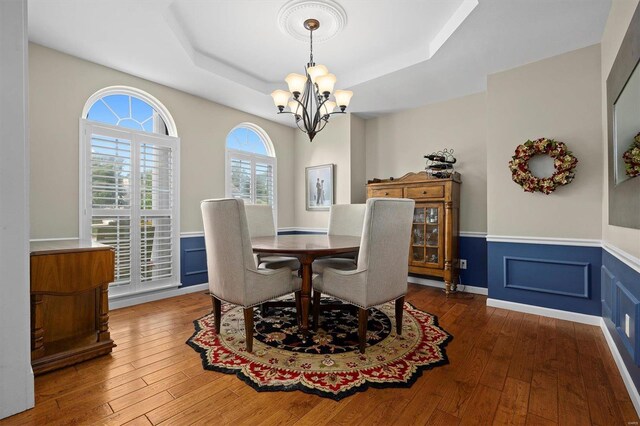 dining space with a notable chandelier, hardwood / wood-style floors, and a raised ceiling