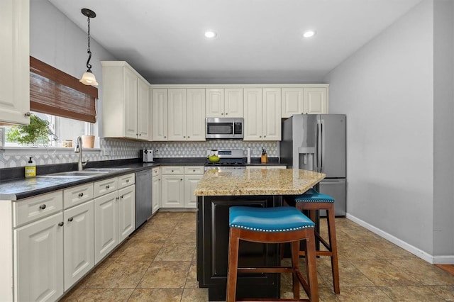 kitchen featuring pendant lighting, stainless steel appliances, dark countertops, a kitchen island, and a sink