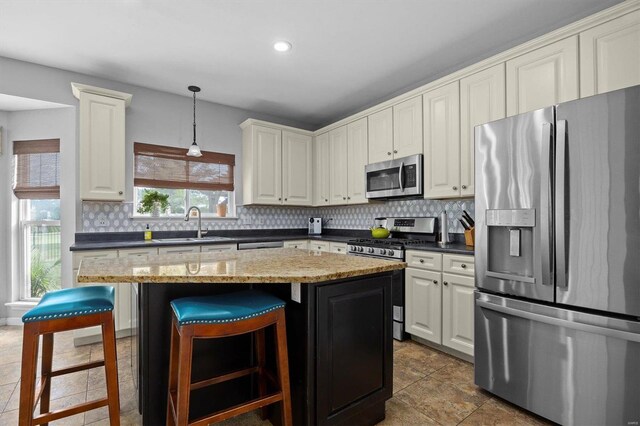 kitchen with dark tile patterned floors, appliances with stainless steel finishes, a center island, decorative light fixtures, and backsplash