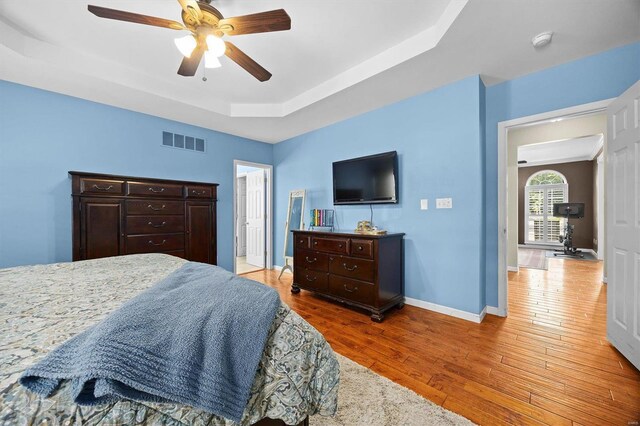 bedroom with ceiling fan, hardwood / wood-style flooring, and a tray ceiling