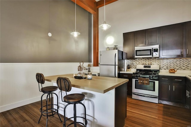 kitchen featuring appliances with stainless steel finishes, a breakfast bar, hanging light fixtures, decorative backsplash, and dark hardwood / wood-style floors