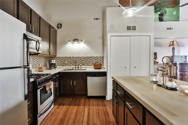 kitchen with stainless steel appliances, sink, dark brown cabinetry, decorative backsplash, and hardwood / wood-style flooring