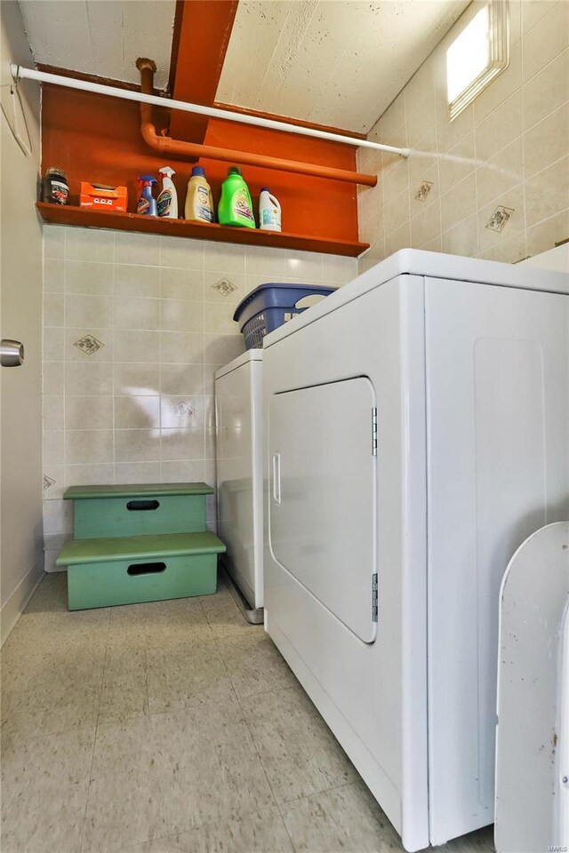 laundry area with tile walls, independent washer and dryer, and light tile patterned floors