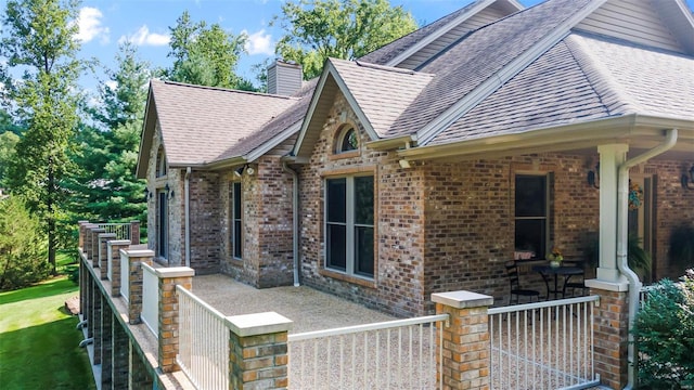 view of property exterior featuring roof with shingles, a chimney, and brick siding