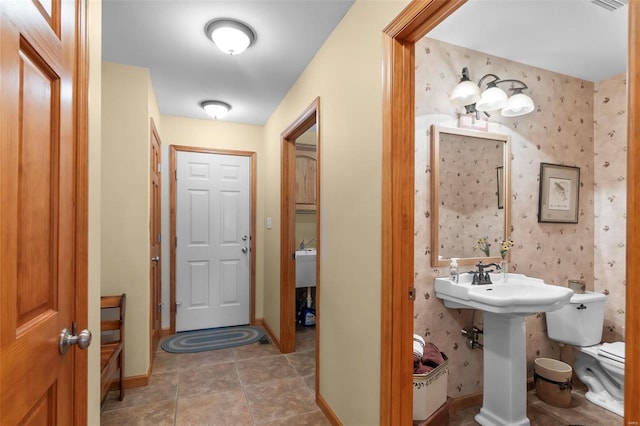 bathroom with tile patterned flooring, toilet, a sink, baseboards, and wallpapered walls