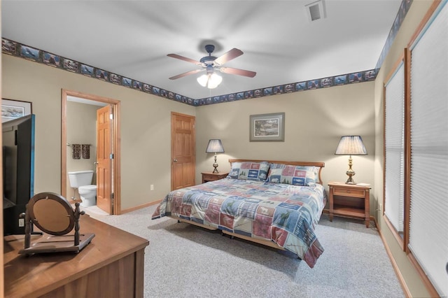 carpeted bedroom with ceiling fan, ensuite bath, visible vents, and baseboards