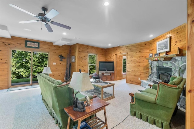 living room with light carpet, wooden walls, a stone fireplace, and recessed lighting