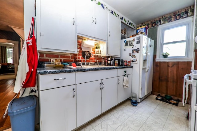 kitchen featuring stove, sink, white refrigerator with ice dispenser, light tile patterned flooring, and white cabinetry