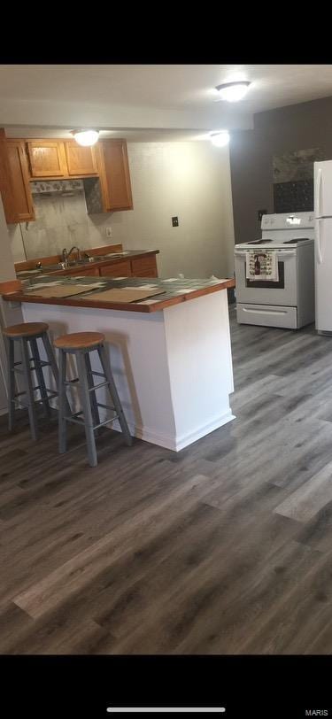 kitchen with dark hardwood / wood-style flooring, a kitchen bar, and white appliances