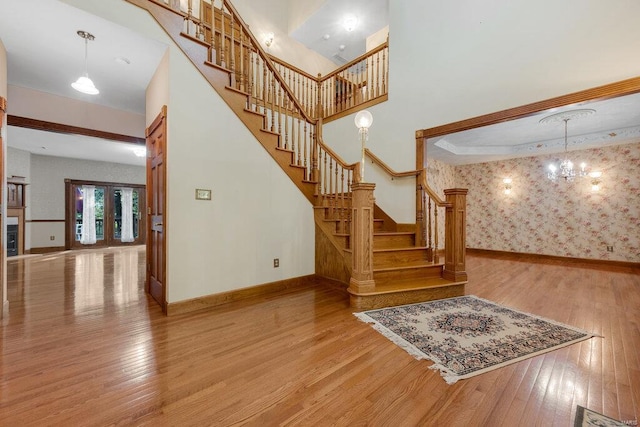 stairs with french doors, a high ceiling, hardwood / wood-style flooring, and a chandelier