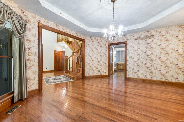 unfurnished dining area featuring hardwood / wood-style floors, a chandelier, and a raised ceiling