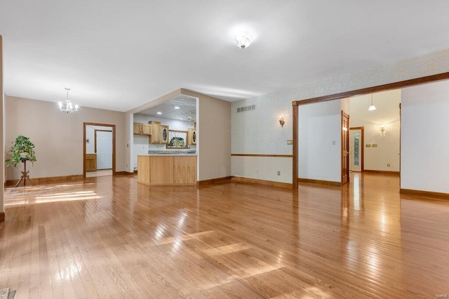 unfurnished living room featuring a chandelier and light hardwood / wood-style floors