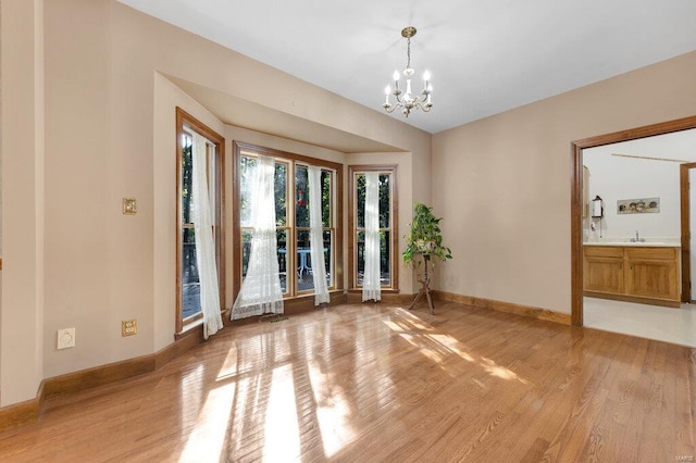 spare room featuring wood-type flooring, sink, and an inviting chandelier