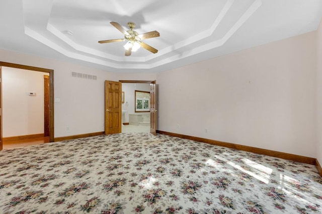 unfurnished bedroom with carpet, ceiling fan, a tray ceiling, and connected bathroom