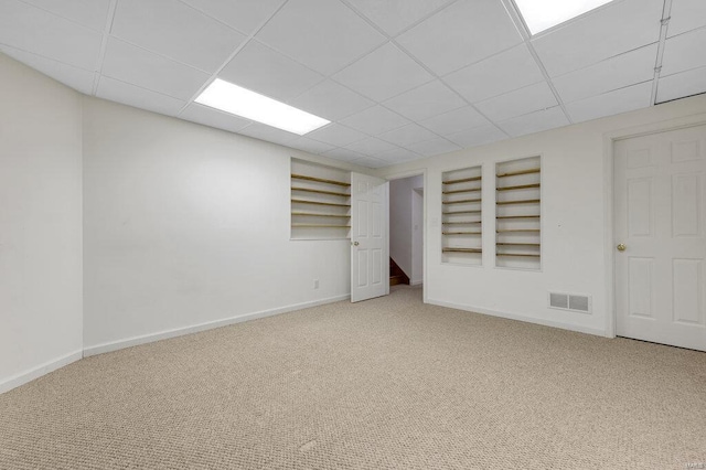 basement featuring a drop ceiling, built in features, and carpet