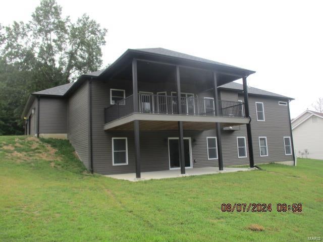 rear view of property featuring a lawn, a balcony, and a patio area