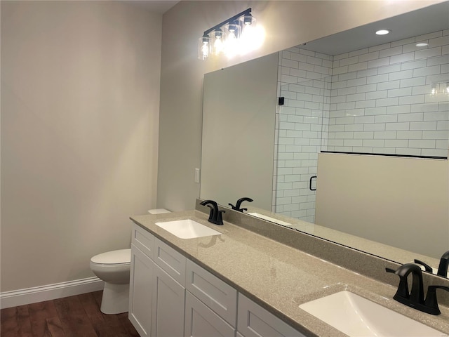 bathroom with toilet, hardwood / wood-style flooring, double sink vanity, and a shower with shower door