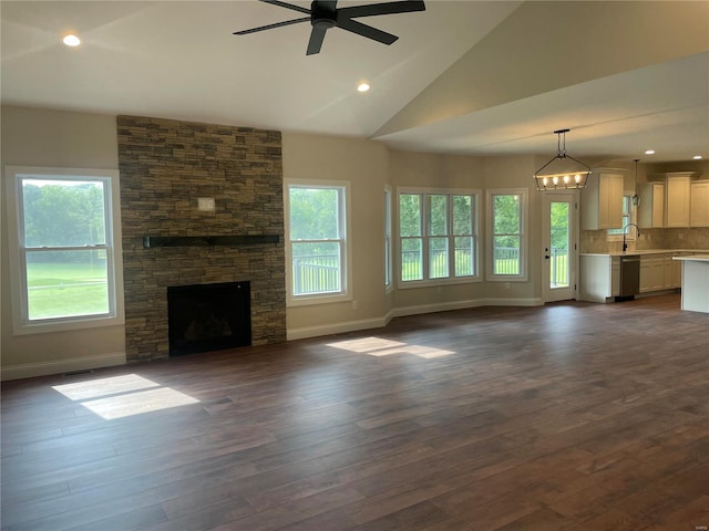 unfurnished living room with ceiling fan, dark wood-type flooring, a stone fireplace, vaulted ceiling, and sink