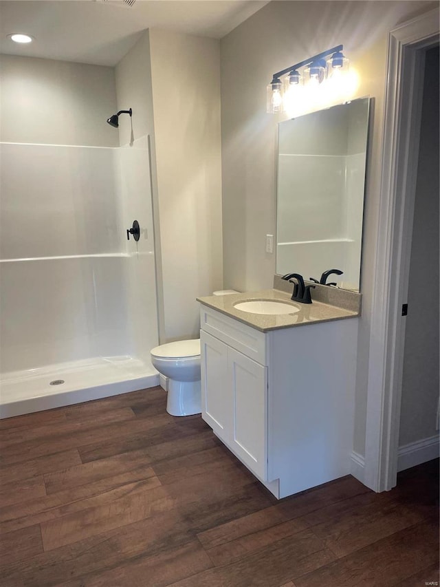 bathroom with hardwood / wood-style flooring, vanity, a shower, and toilet