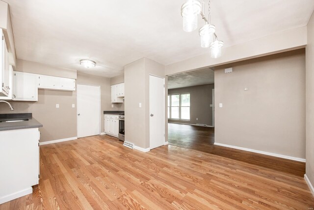 kitchen featuring pendant lighting, white cabinets, sink, light wood-type flooring, and stainless steel range