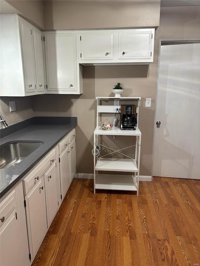 kitchen with wood-type flooring, white cabinetry, and sink