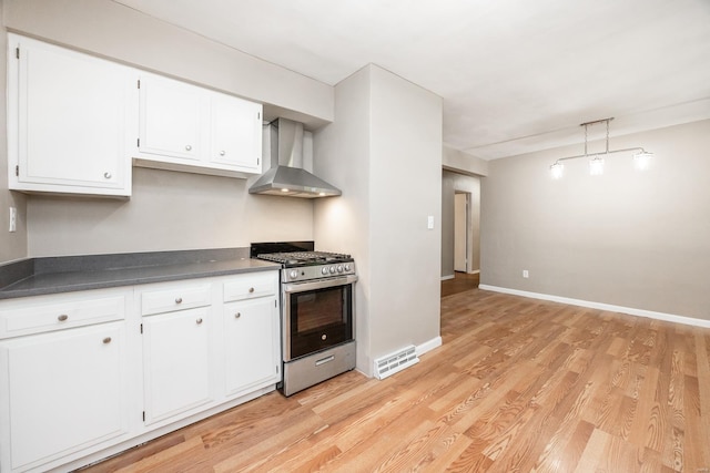 kitchen with light wood-type flooring, white cabinetry, wall chimney exhaust hood, and stainless steel gas range