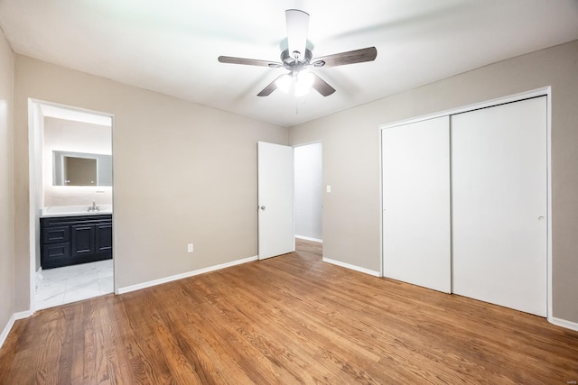 unfurnished bedroom featuring light wood-type flooring, ceiling fan, sink, connected bathroom, and a closet