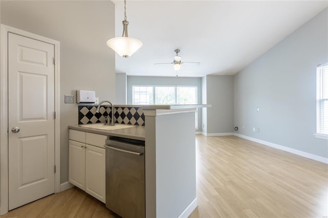 kitchen with kitchen peninsula, light wood-type flooring, decorative light fixtures, stainless steel dishwasher, and sink