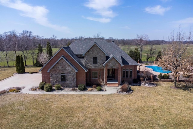 view of front of house featuring a shingled roof, a front lawn, concrete driveway, stone siding, and brick siding