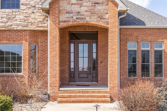 doorway to property with brick siding and roof with shingles