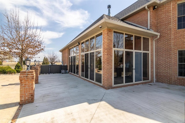 rear view of house with brick siding, a sunroom, and a shingled roof