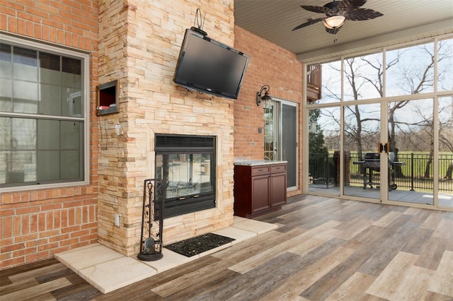 unfurnished living room featuring an outdoor stone fireplace, wood finished floors, a ceiling fan, and brick wall