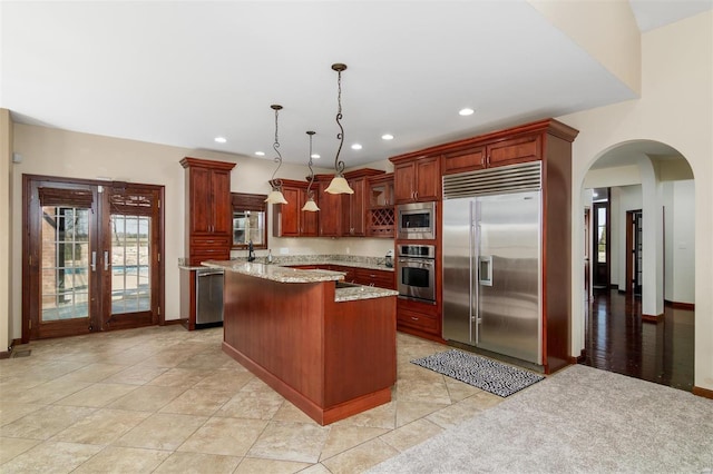 kitchen featuring recessed lighting, arched walkways, hanging light fixtures, built in appliances, and a center island