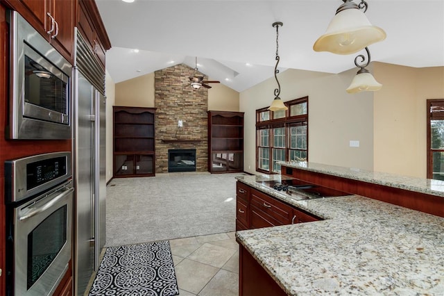 kitchen with ceiling fan, built in appliances, light colored carpet, a fireplace, and reddish brown cabinets