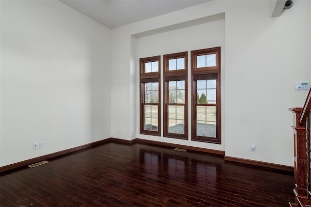 empty room with visible vents, baseboards, and dark wood finished floors