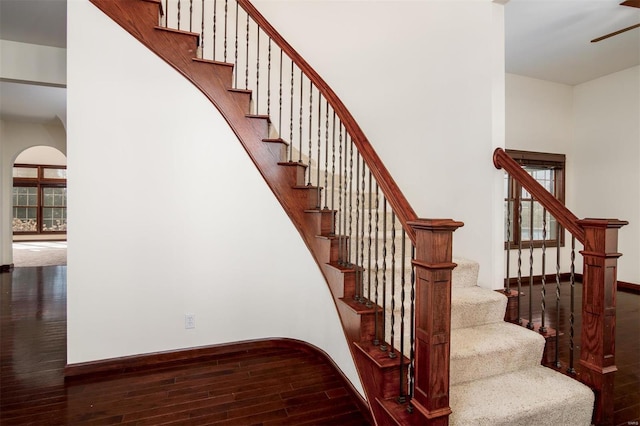 stairway featuring wood finished floors, arched walkways, and baseboards