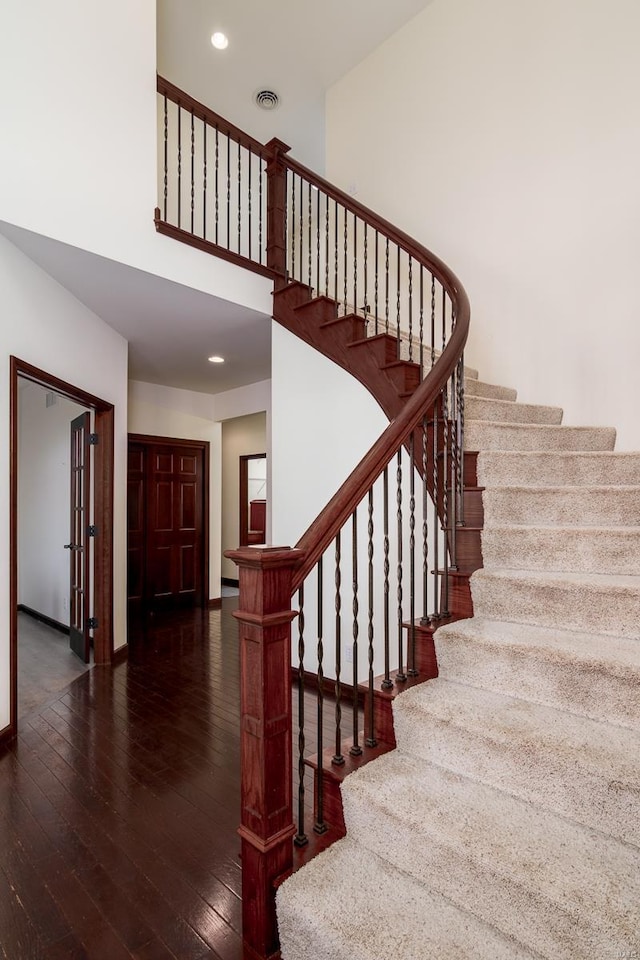 stairway featuring visible vents, baseboards, a high ceiling, recessed lighting, and wood-type flooring