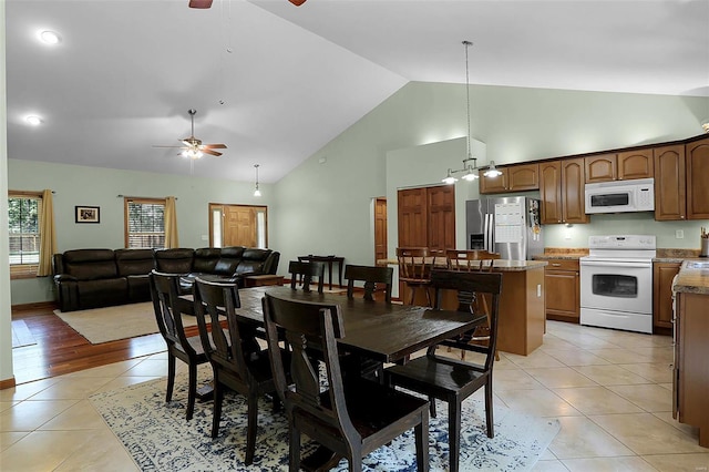 dining area with light tile patterned flooring, ceiling fan with notable chandelier, and high vaulted ceiling