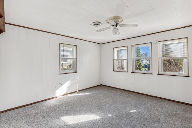 carpeted empty room featuring ceiling fan, ornamental molding, a wealth of natural light, and baseboards