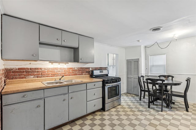 kitchen with backsplash, stainless steel gas stove, gray cabinets, and sink