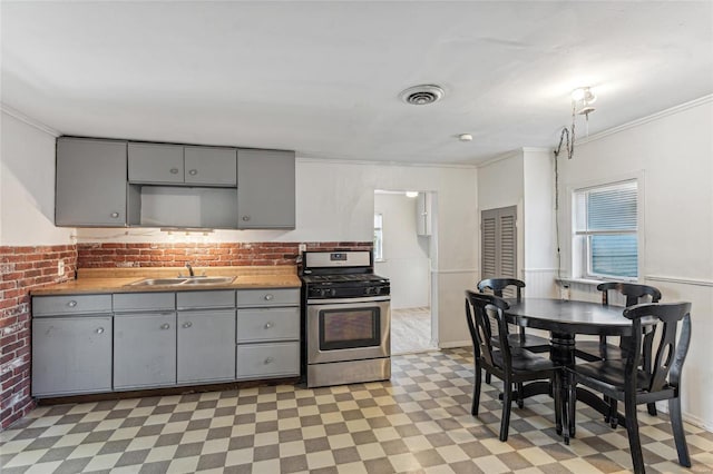 kitchen with stainless steel gas range oven, sink, gray cabinets, and ornamental molding