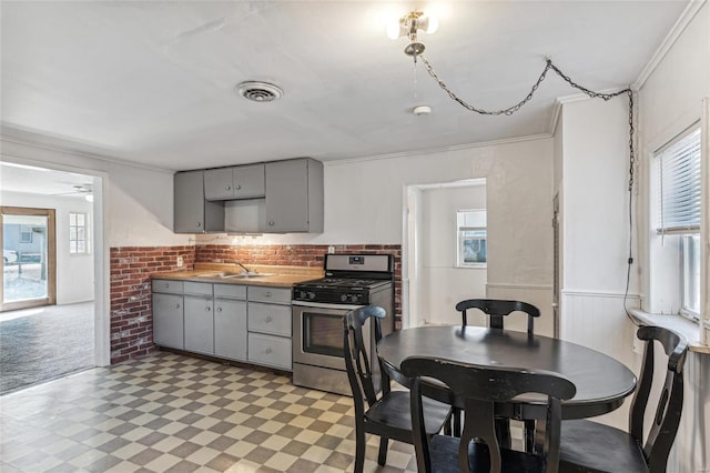 kitchen with stainless steel gas stove, light floors, a sink, and gray cabinetry