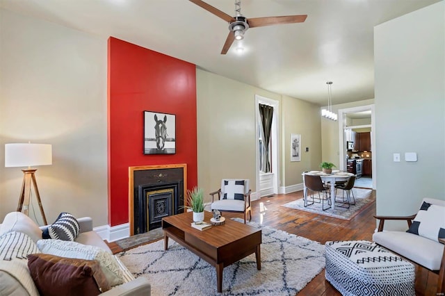 living room featuring ceiling fan, a fireplace, dark wood-type flooring, and baseboards