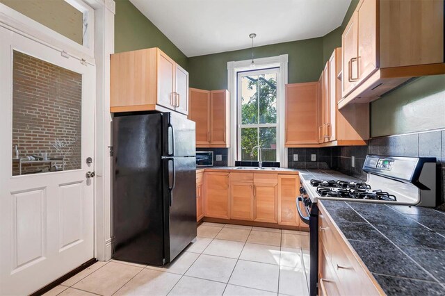 kitchen featuring black fridge, hanging light fixtures, light tile patterned flooring, and white gas range oven