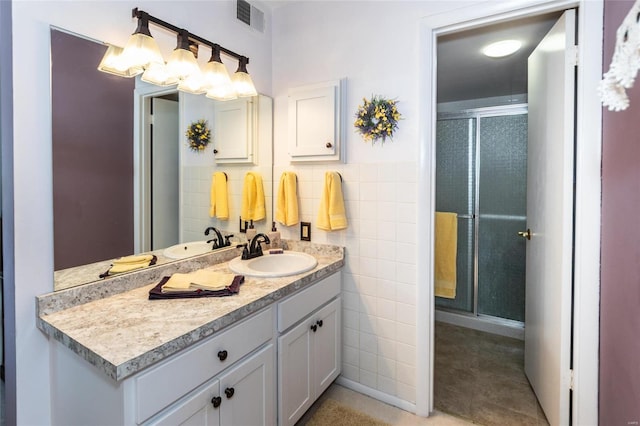 bathroom with tile walls, tile patterned flooring, a shower with door, and vanity