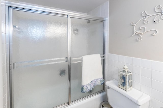 bathroom featuring enclosed tub / shower combo, toilet, and tile walls