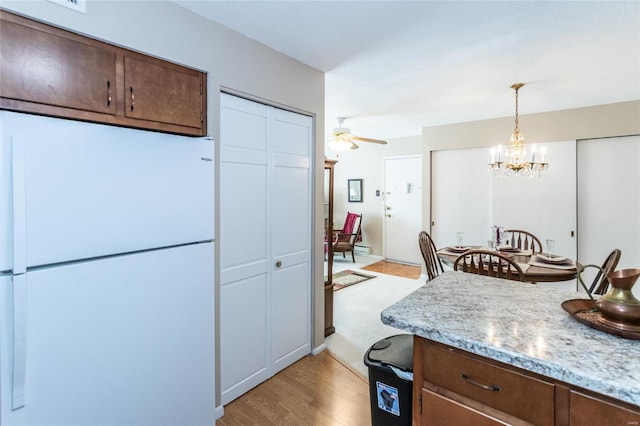 kitchen with decorative light fixtures, dark brown cabinetry, white fridge, ceiling fan with notable chandelier, and light carpet