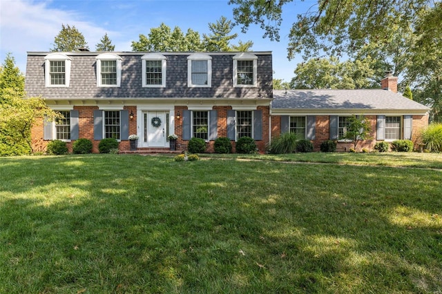 front facade featuring mansard roof, brick siding, a front lawn, and roof with shingles