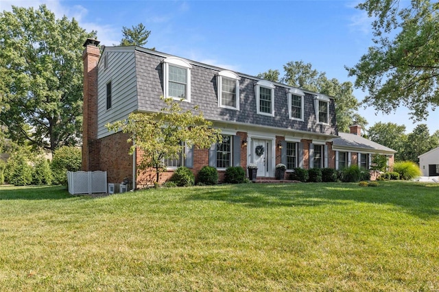 view of front of house with brick siding, a shingled roof, mansard roof, a chimney, and a front yard